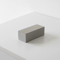 Minimalist concrete paperweight with a brass inlay line on a white desk, soft studio light