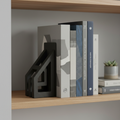 A pair of matte-black architectural cast-metal bookends holding design books on a shelf, soft light